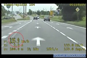 Kadr z filmu przedstawiający, jak kierowca samochodu osobowego przekracza prędkość jadąc 135 kilometrów na godzinę w terenie zabudowanym