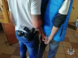 Nieumundurowany policjant prowadzi zatrzymanego w kajdankach  do aresztu
