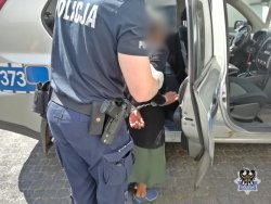 Zatrzymana kobieta wprowadzana przez policjanta do radiowozu