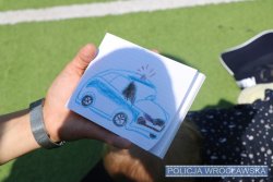 Na zdjęciu ręka trzyma kartkę, na której narysowany jest policyjny radiowóz
