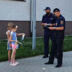 Policjanci rozdają ulotki na temat bezpiecznych wakacji i rozmawiają z napotkanymi dziewczynkami