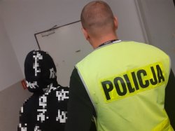 Policjant prowadzi zatrzymaną kobietę ubraną w bluzę z kapturem na głowie