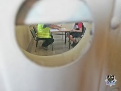Na zdjęciu policjant podczas przesłuchania zatrzymanego mężczyzny. Zdjęcie zrobione przez wizjer w drzwiach do pokoju.