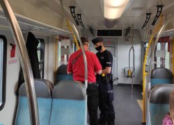 Policjant w maseczce ochronnej w pociągu rozmawia z kierownikiem pociągu.