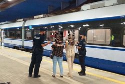 Policjant z policjantką w maseczkach ochronnych rozmawiają z dwiema pasażerkami, na peronie kolejowym. w tle pociąg.