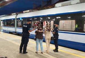 Policjant z policjantką w maseczkach ochronnych rozmawiają z dwiema pasażerkami, na peronie kolejowym. w tle pociąg.