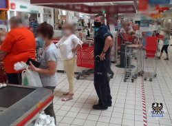 Na zdjęciu policjant, który w placówce handlowej kontroluje przy kasach sklepowych klientów i kasjerów czy posiadają maseczki i czy zachowują wymagany odstęp.