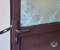 Na zdjęciu uszkodzone drzwi do budynku, widać stłuczoną szybę.