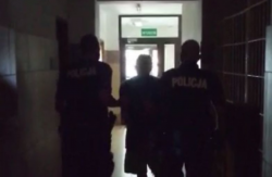 Dwaj policjanci prowadzą zatrzymanego mężczyznę korytarzem na komendzie policji
