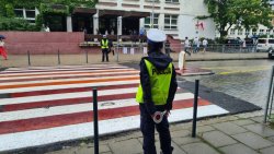 Umundurowani Policjanci pilnują bezpieczeństwa na oznakowanym przejściu dla pieszych przy szkole.