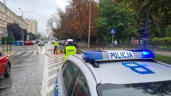 policjanci przy radiowozie ustawionym przy drodze kierują ruchem na przejściu dla pieszych przy szkole.