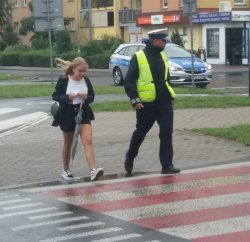 policjant pomaga bezpiecznie przejść dziewczynce na drugą stronę jezdni