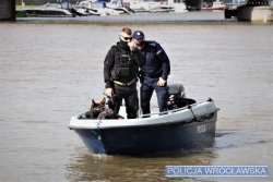 Na zdjęciu Policjanci Komisariatu Wodnego wraz z psem policyjnym znajdują się na łódce i przeszukują rzekę.