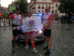 Wspólne zdjecie uczestników biegu z flagą na tle radiowozu