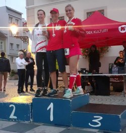 Uczestnicy Biegu stojący na podium pokazują pamiątkowe medale.