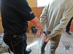 Policjant prowadzi zatrzymanego w kajdankach do aresztu