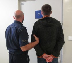 zatrzymany stoi wraz z policjantem na tle jasnej ściany