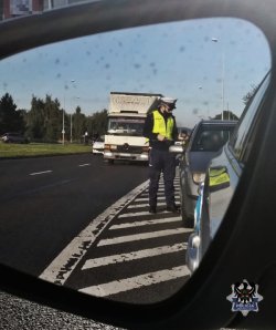 Odbicie w lusterku policjanta który rozmawia z kierowcą podczas kontroli drogowej