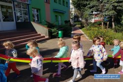 dzieciaki idą bezpiecznie z przedszkola na spacer trzymając kolorową dżownicę