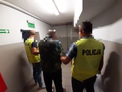 nie umundurowani policjanci prowadzą korytarzem jednego z 2 mężczyzn zatrzymanych za atak na policjantów
