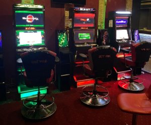 zabezpieczone automaty do gier hazardowych które stały w salonie gier. Przed nimi stoją krzesła obrotowe.