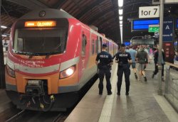 Policjanci stojący na peronie obok pociągu, w tle wysiadający z pociągu pasażerowie