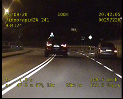 Zdjęcie z wideorejestratora przedstawiające kierowcę samochodu osobowego wyprzedzającego nieprzepisowo inny pojazd znajdujący się na zakręcie