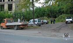 Na zdjęciu miejsce dewastacji pojazdów w Jedlinie-Zdroju, w tle samochody i policjanci z zatrzymanym.