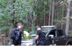 Na zdjęciu policjant obok samochodu straży leśnej wypisuje mandat stojącemu obok kierowcy motocykla.