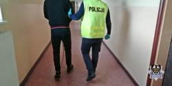 Na zdjęciu policjant prowadzi zatrzymanego mężczyznę korytarzem w komendzie policji.