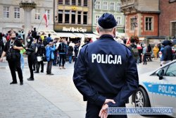 Zdjęcie przedstawia policjanta stojącego tyłem, w tle znajdują się demonstranci