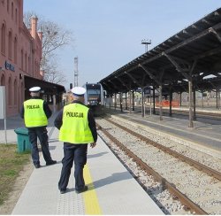 Na zdjęciu dwóch policjantów na peronie kolejowym. Widać nadjeżdżający pociąg na stację.