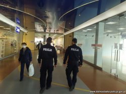 Na zdjęciu widać idących policjantów na tle sklepów jednej z galerii handlowych. Po lewej stronie idzie osoba z białą torbą w ręce.