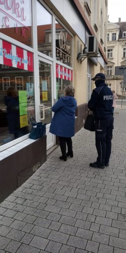 Zdjęcie przedstawia policjanta w mundurze, który stoi wraz z kobietą przy budynku.