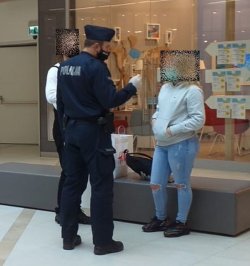Na zdjęciu policjant rozmawia z dwiema kobietami koło centrum handlowego. Wszyscy na zdjęciu mają maseczki ochronne na twarzy.
