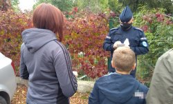 Na zdjęciu policjant, który rozmawia z kobietą i chłopcem, obok widać ramię mężczyzny. Policjant i kobieta mają na twarzy maseczki.
