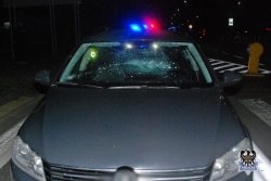 Na zdjęciu nocną porą widzimy przód uszkodzonego samochodu osobowego. W dali widać sygnalizację świetlną radiowozu policyjnego.