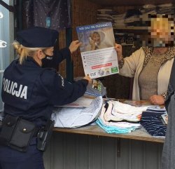 Na zdjęciu policjantka przekazuje materiały prewencyjne dotyczące bezpieczeństwa seniorów sprzedawczyni na stoisku targowym.