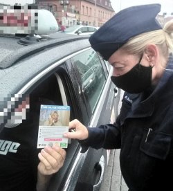 Na zdjęciu policjantka przekazuje materiały prewencyjne dotyczące bezpieczeństwa seniorów taksówkarzowi siedzącemu w samochodzie.