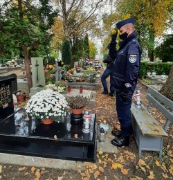 Na zdjęciu salutujący policjant, oddający hołd nad grobem bohaterów walk Powstania Wielkopolskiego i wojny polsko - bolszewickiej. Na grobie widoczne są złożone kwiaty i znicze.