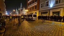 Na zdjęciu widać rynek wrocławski, a przy jednej z kamienic stoją umundurowani policjanci. Widać także inne postronne osoby oraz zaparkowane radiowozy policyjne.