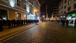 Przy jednej z wrocławskich kamienic w rynku stoją umundurowani policjanci. Widać także postronne osoby i radiowozy policyjne z włączonymi sygnałami błyskowymi barwy niebieskiej. W tle okoliczne zabudowania.