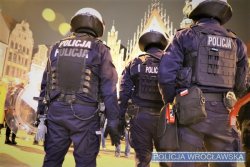 Trzech umundurowanych policjantów w kaskach ochronnych na tle wrocławskiego rynku.