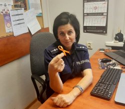 Na zdjęciu policjantka siedząca przy biurku i trzymająca w ręku pomarańczową wstążkę