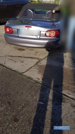 Na zdjęciu widok z tyłu zaparkowanego pod płotem samochodu marki Mazda wersja Kabrio. Numery Rejestracyjne zamazane.