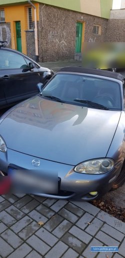 Na zdjęciu widok z przodu zaparkowanego pod płotem samochodu marki Mazda wersja Kabrio. Numery Rejestracyjne zamazane.