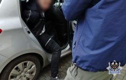 Na zdjęciu policjant umieszcza pierwszego z zatrzymanych mężczyzn w radiowozie.