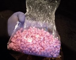Na zdjęciu policjant trzymający woreczek z różowymi tabletkami.