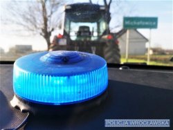 Zdjęcie przedstawia policyjną lampę koloru niebieskiego oraz ciągnik rolniczy.
