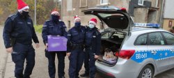 Troje policjantów w czapkach Świętego Mikołaja stoją z prezentami koło radiowozu.